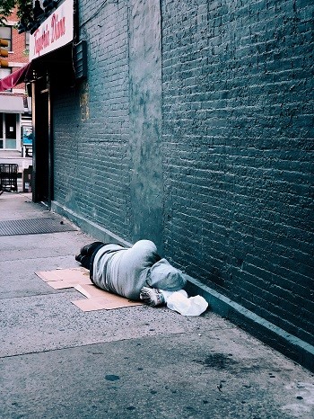 Un hombre sin hogar yace solo en la calle junto a una pared de ladrillos desnudos.