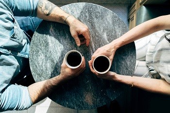 Mirando hacia abajo en una mesa redonda, dos pares de brazos sostienen tazas de café