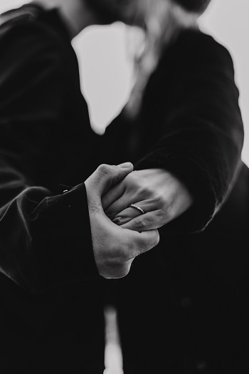 Una pareja se toma de la mano mientras se besa, caras fuera del marco